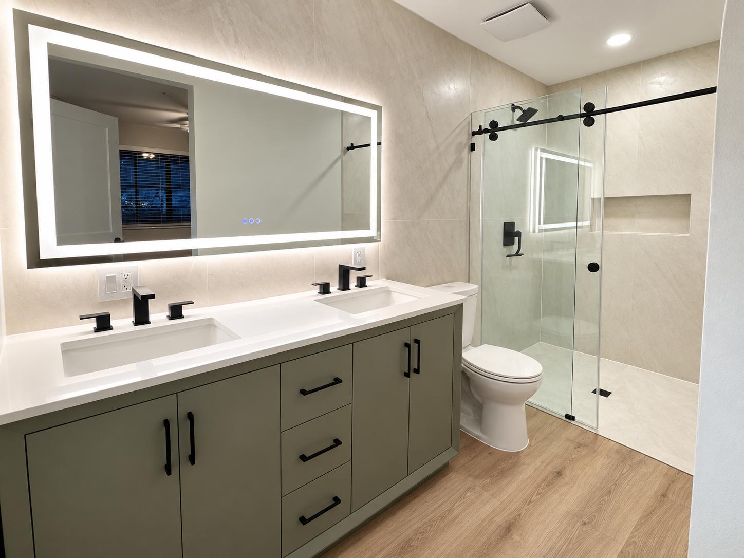 Remodeled bathroom with a double vanity, lit mirror, and walk-in shower with sliding glass door